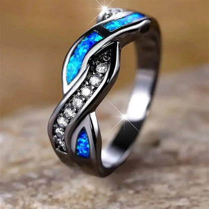 Bague Thessia Lunebray noire, deux inserts bleu opale et ailettes serties de pierres claires.