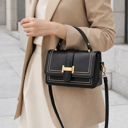 Sac à main en cuir noir porté à l’épaule, rabat à fermoir doré et surpiqûres.