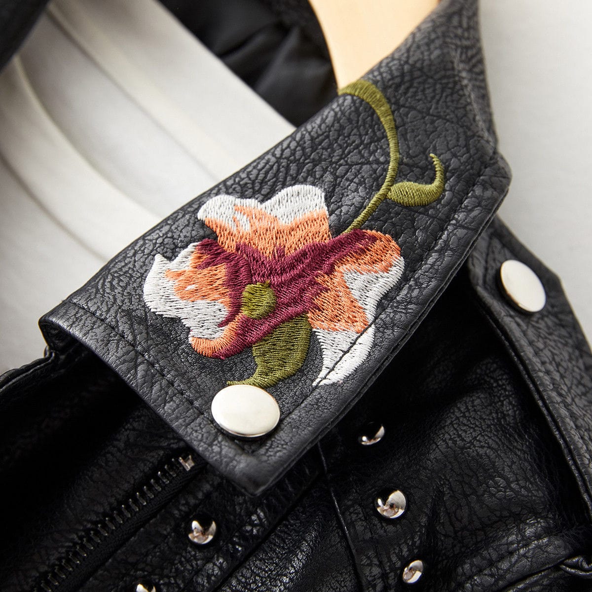 Veste en cuir noir, bracelet d’épaule avec broderie florale et boutons ronds.