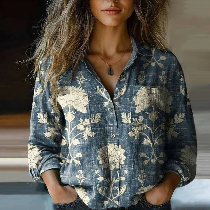 Chemisier vintage bleu à boutons, col ouvert, imprimé floral blanc, manches longues retroussées.