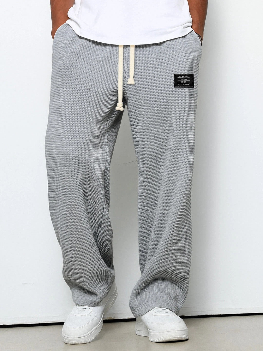 Pantalon ample gris à taille élastique et cordon, étiquette rectangulaire sur la hanche.
