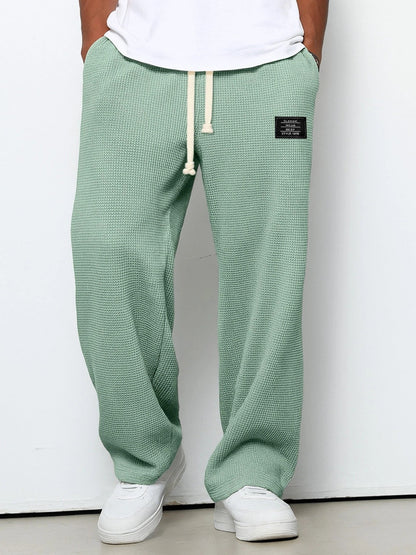 Pantalon ample vert clair à taille élastique et cordon, étiquette sur la hanche droite.