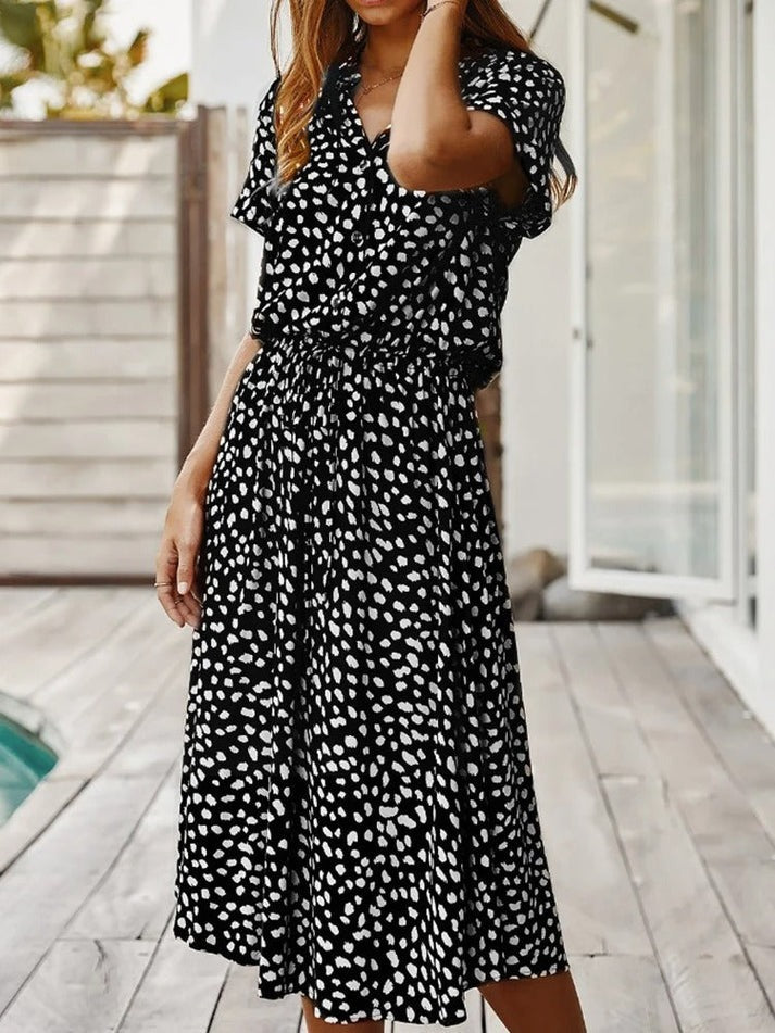 Robe fluide midi noire à motifs taches blanches, col V, ceinture froncée, manches courtes.