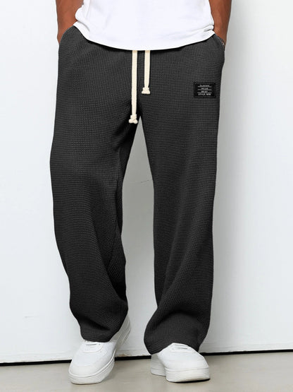 Pantalon large noir à taille réglable, cordon à la ceinture, jambe ample, tissu texturé.