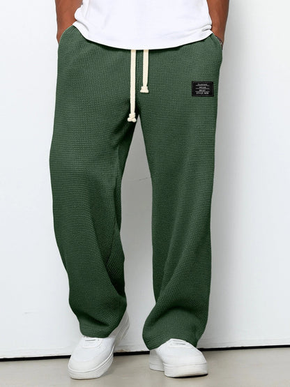 Pantalon large vert foncé à taille réglable, cordon à la ceinture, jambe ample, tissu texturé.