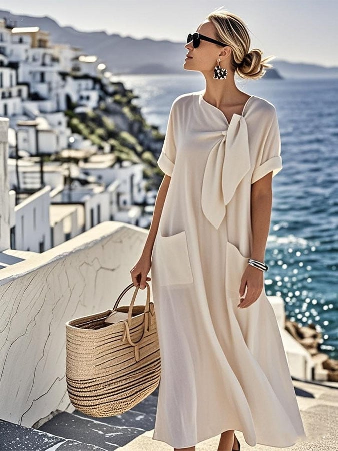 Robe ample en coton beige clair, manches courtes, nœud au col, poches avant discrètes.