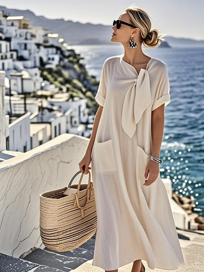 Robe ample en coton beige clair, manches courtes, nœud au col, poches avant discrètes.