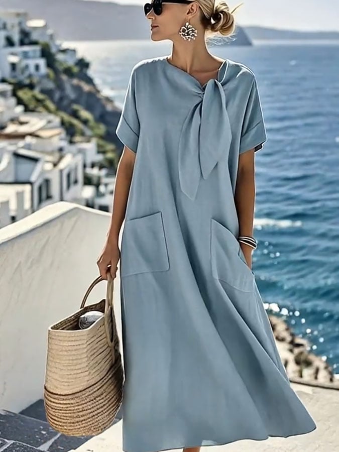 Robe en coton bleu clair avec nœud tombant, manches courtes, poches plaquées sur la poitrine.