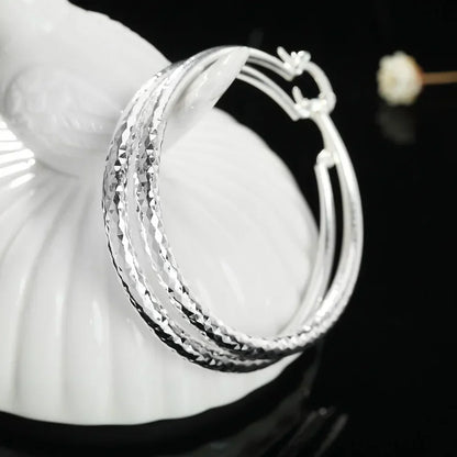 Boucles d’oreilles créoles en argent, gros plan sur la texture losangée de l’anneau.