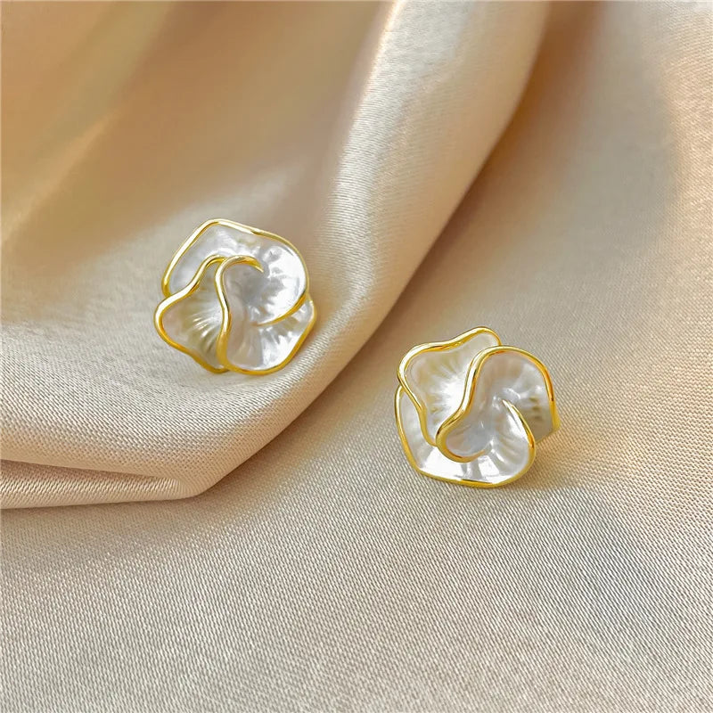 Boucles d’oreilles fleurs en perles blanches et monture dorée, posées sur tissu