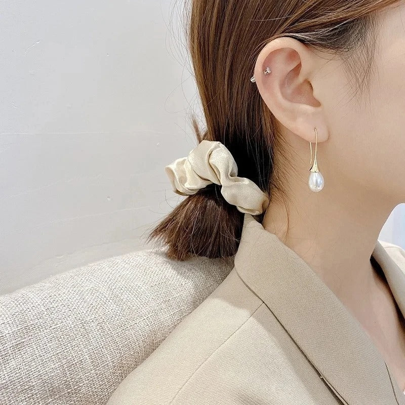 Boucle d’oreille pendante dorée avec perle goutte blanche, portée sur l’oreille