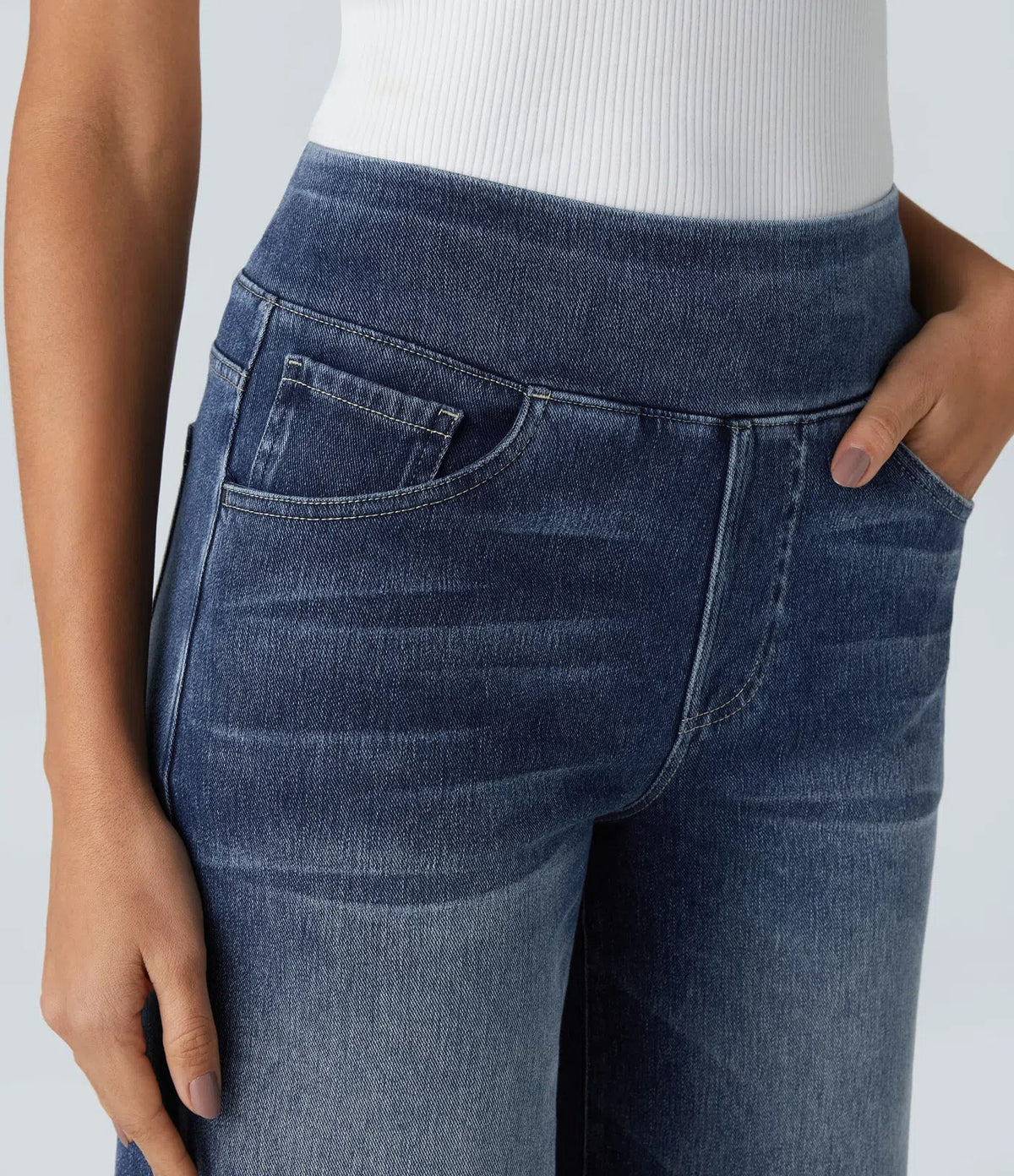 Pantalon en jean bleu, ceinture boutonnée, poches avant et surpiqûres visibles.
