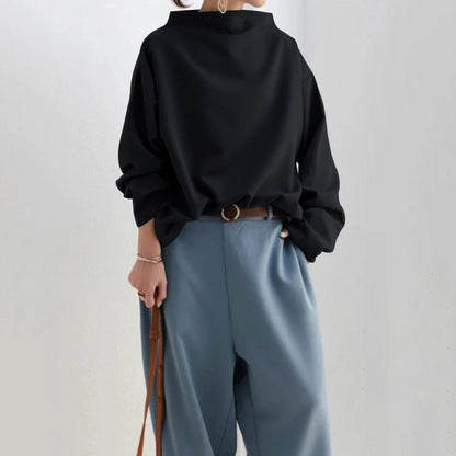 Haut noir à col cheminée, manches amples bouffantes, porté avec pantalon clair