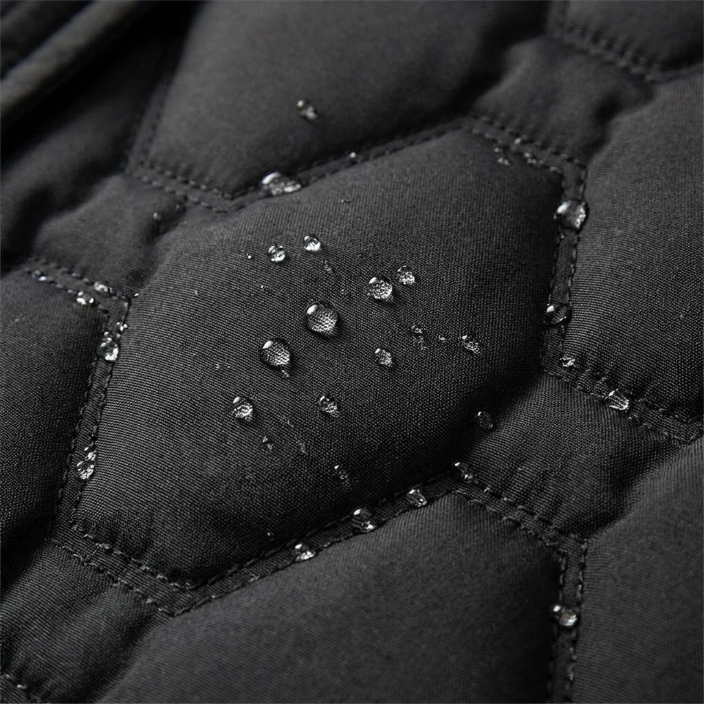 Manteau long imperméable noir matelassé, gouttes d’eau visibles sur les coutures.