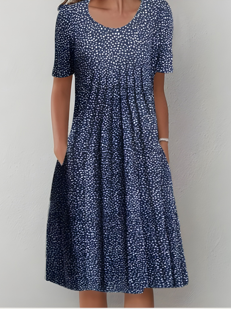 Robe plissée bleu foncé à petits pois blancs, manches courtes, encolure ronde.