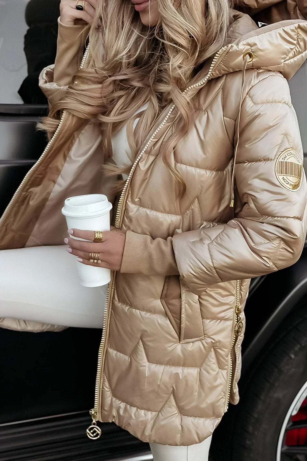 Manteau matelassé beige à capuche, zip doré, écusson sur la manche, manches longues.