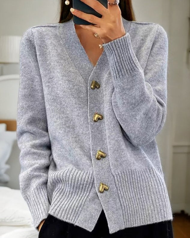 Gilet doux gris à encolure en V, boutons en forme de cœur dorés, manches longues.