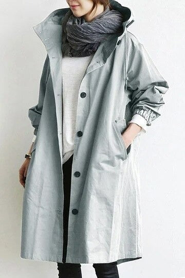 Trench-coat déperlant long gris clair à capuche, patte boutonnée, poches latérales.