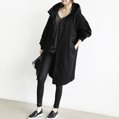 Trench-coat déperlant long noir à capuche, patte boutonnée, poches latérales.