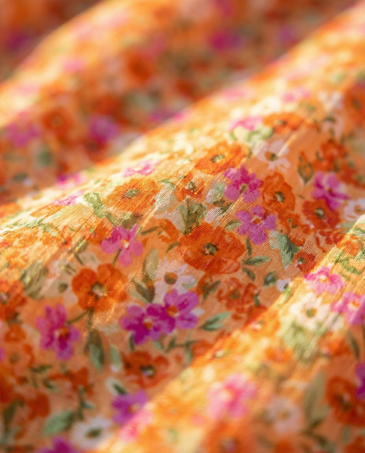 Détail tissu robe d’été : motif fleuri multicolore sur fond orange