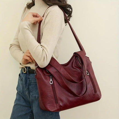 Sac à bandoulière en cuir rouge bordeaux, porté en bandoulière avec anneaux métalliques
