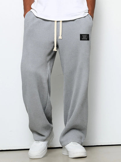Pantalon pour hommes à coupe confortable gris, taille à cordon, devant fendu, étiquette.