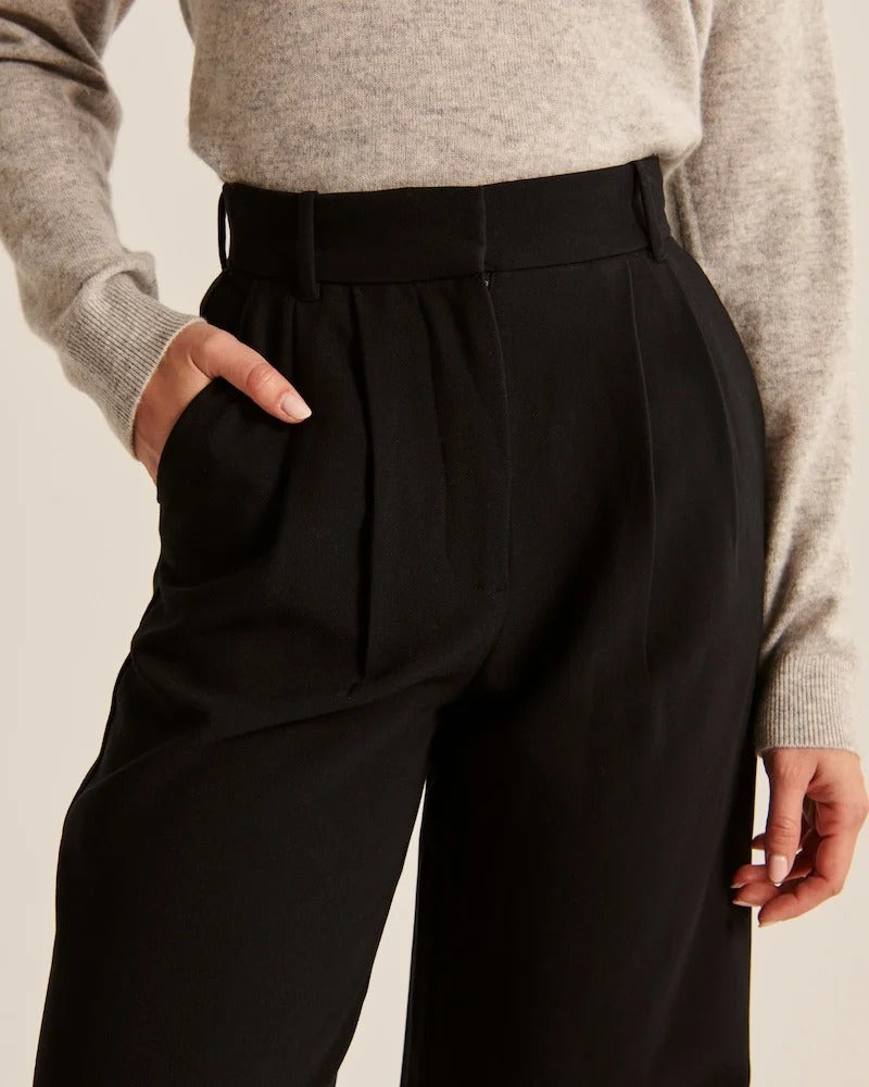 Pantalon noir taille haute à pinces, poches discrètes et fermeture à bouton.