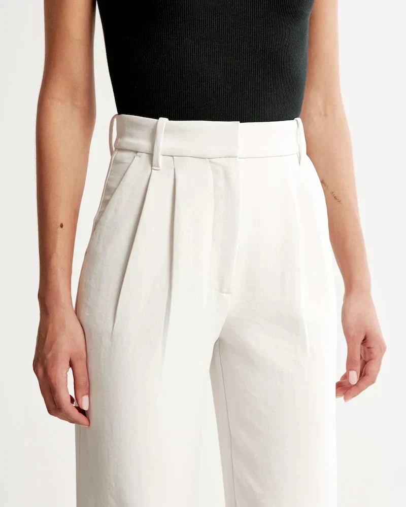Pantalon blanc taille haute, pinces et passants de ceinture, fermeture à bouton.
