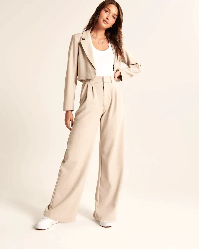 Pantalon beige taille haute à pinces, jambes larges, passants de ceinture et poches.