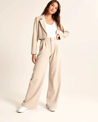 Pantalon beige taille haute à pinces, jambes larges, passants de ceinture et poches.