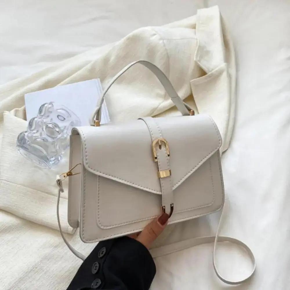 Sac à bandoulière blanc cassé avec rabat et fermoir doré, anse courte et bandoulière.