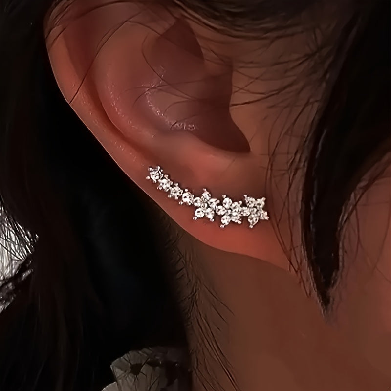 Boucles d’oreilles fleurs en strass blanc, motif dentelé, portées sur l’oreille.