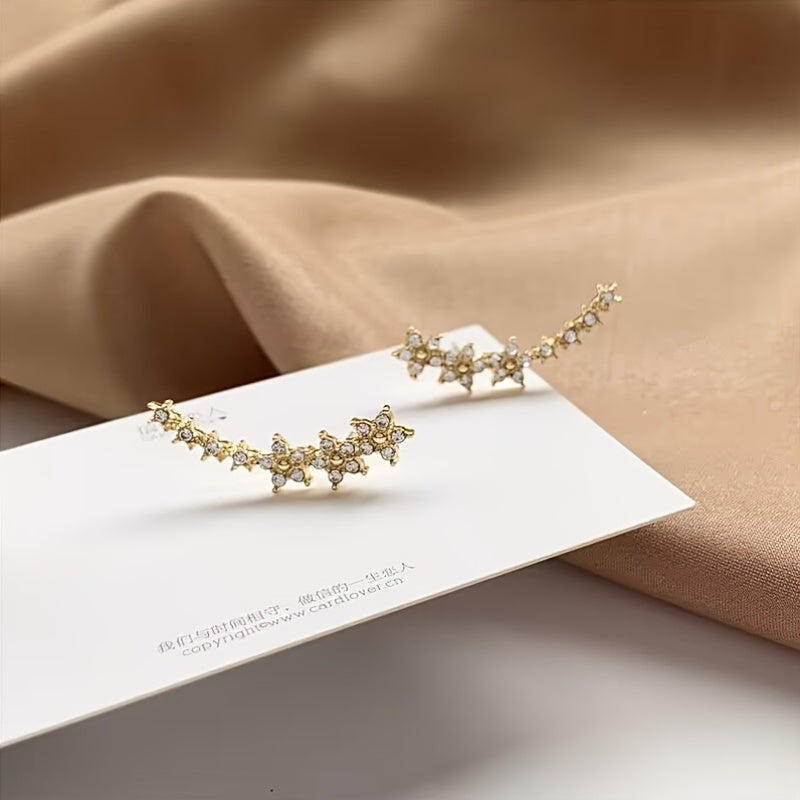 Boucles d’oreilles fleurs en strass doré, motif en rangée, posées sur carte.