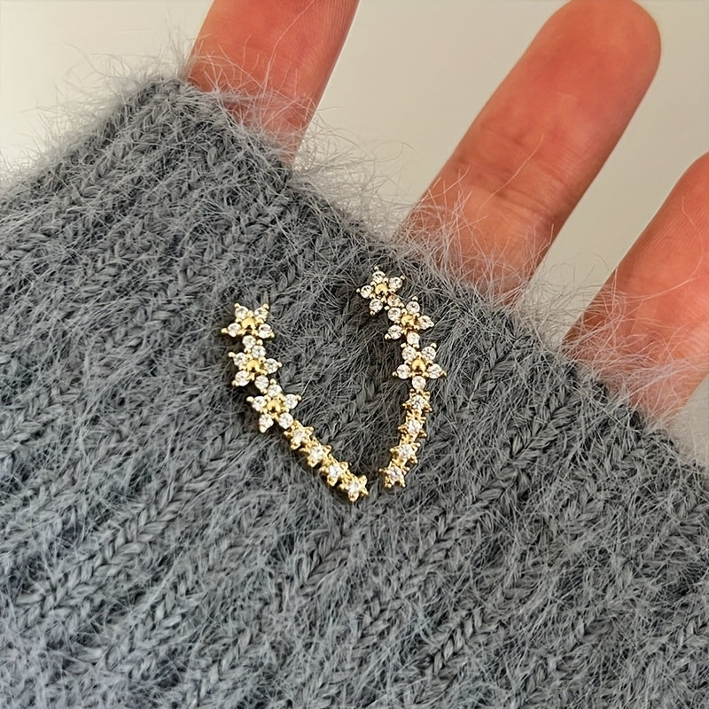Boucles d’oreilles fleurs en strass doré, portées, forme en U avec rangée de strass.