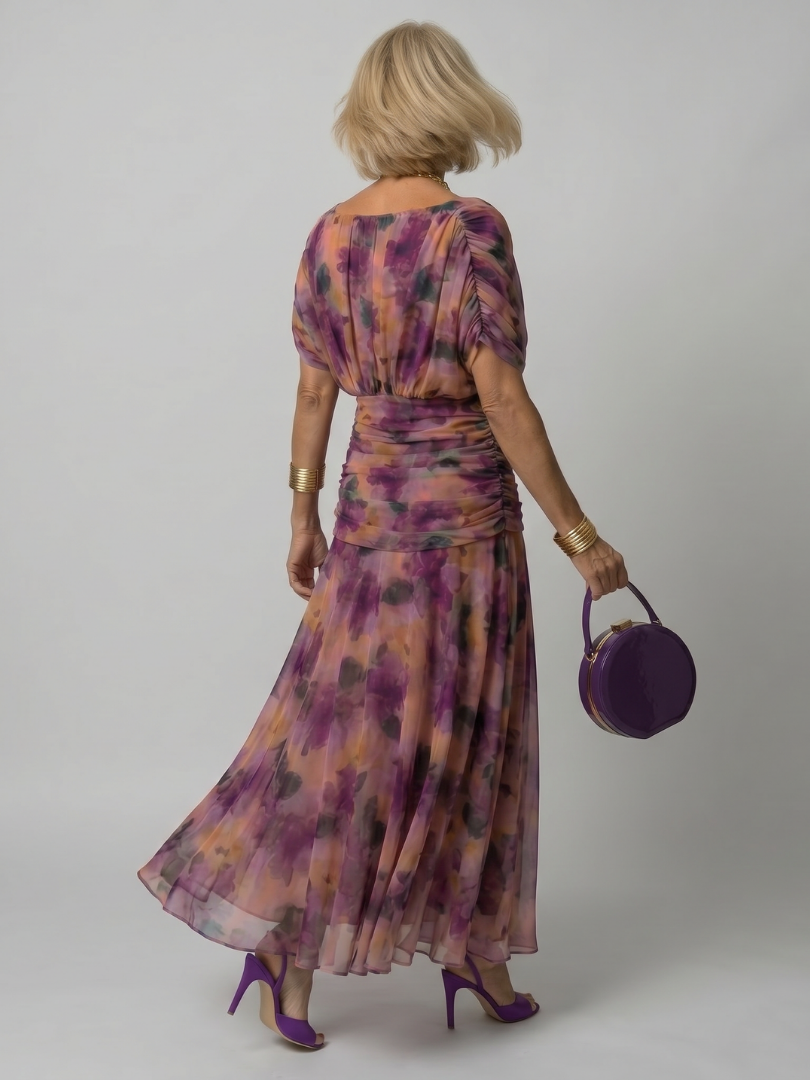 Robe longue violette à fleurs, dos élastiqué, jupe évasée et manches courtes.