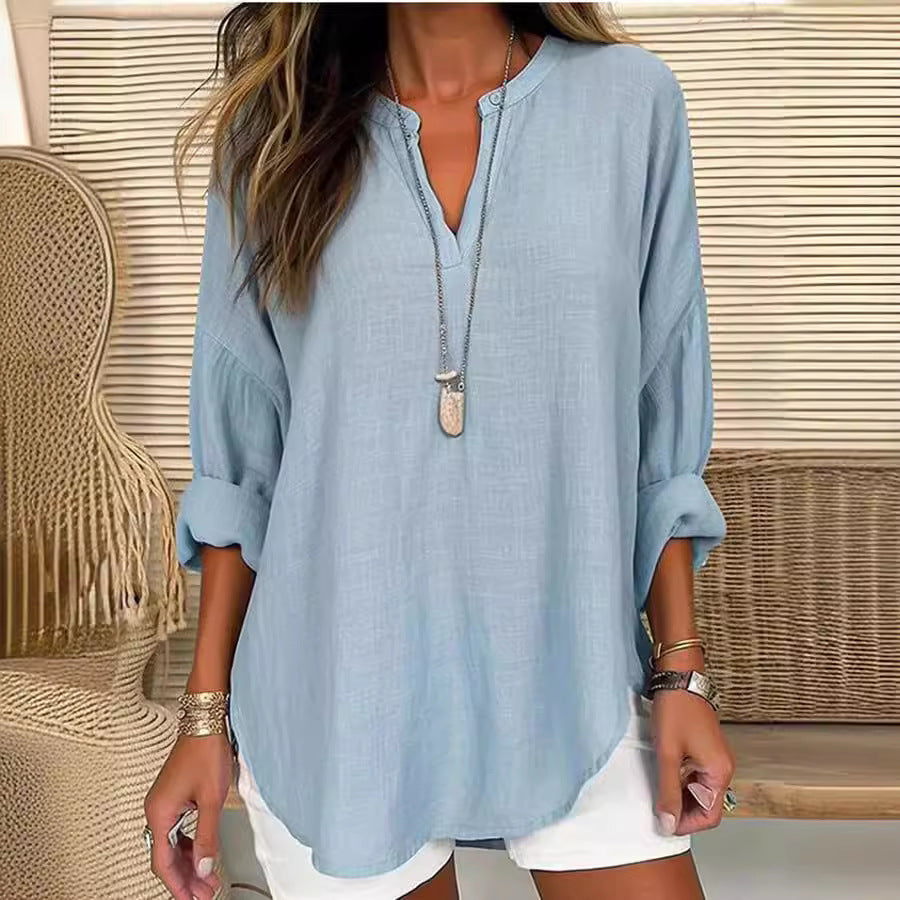 Blouse ample bleu clair, encolure V boutonnée, manches trois-quarts retroussées.