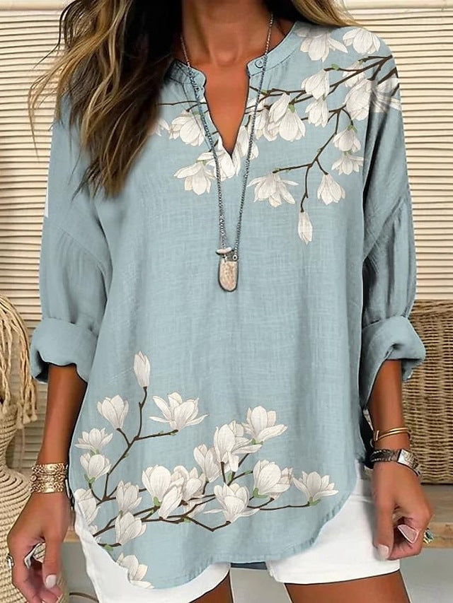 Blouse ample bleu clair à fleurs blanches et encolure V boutonnée, manches trois-quarts.