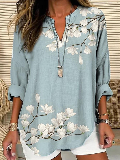Blouse ample bleu clair à fleurs blanches et encolure V boutonnée, manches trois-quarts.
