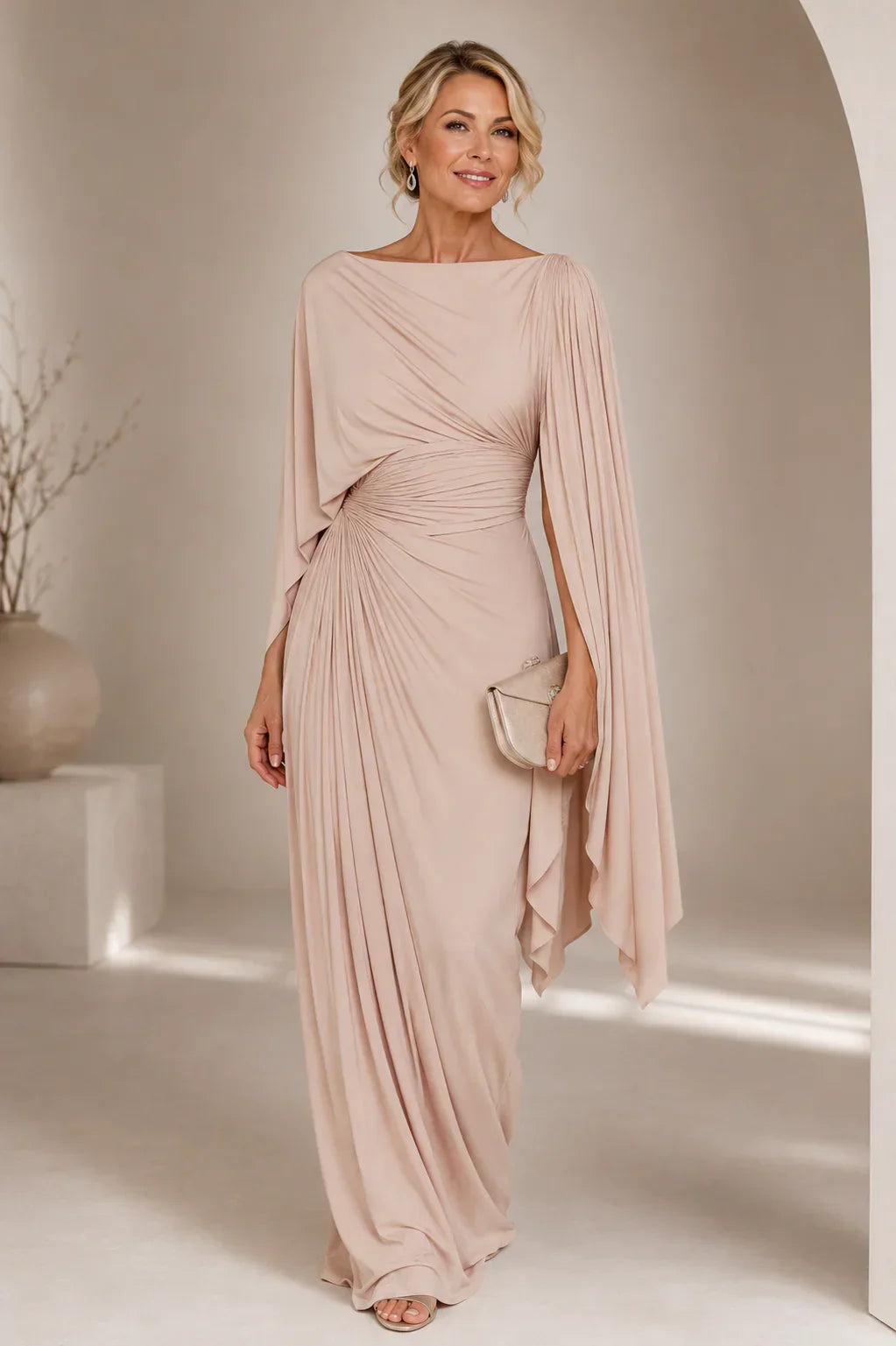 Robe longue plissée rose poudré, manches longues ample cape, drapée sur le devant, fente latérale.