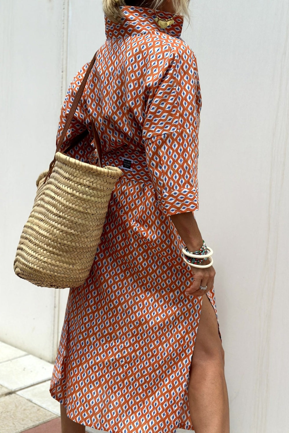 Robe chemise orange et blanc à motifs, col ouvert, fente sur le côté, manches trois-quarts.