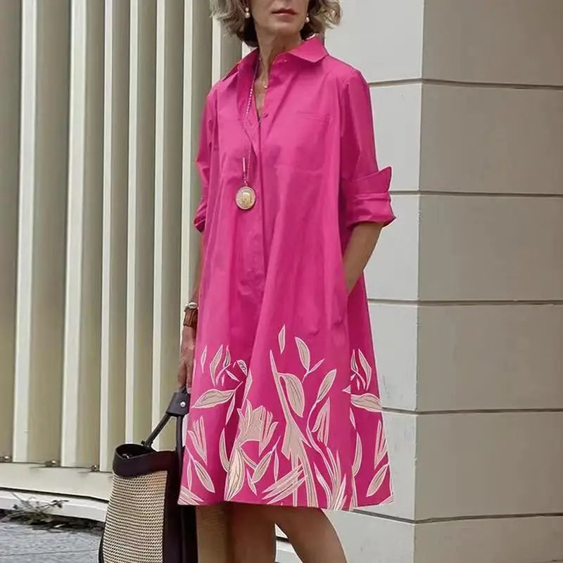 Robe mi-longue fuchsia à col chemise, manches retroussées, bas imprimé feuillagé blanc.
