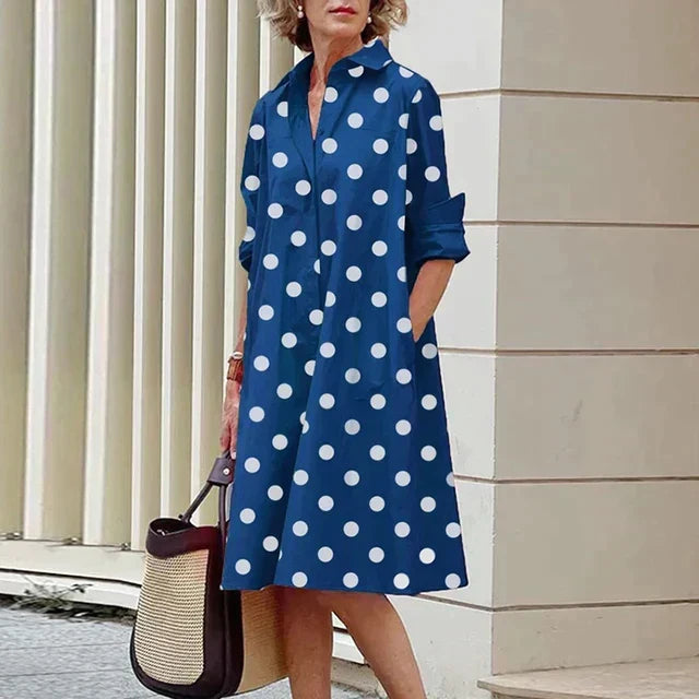 Robe bleue mi-longue à pois blancs, col chemise, manches trois-quarts.