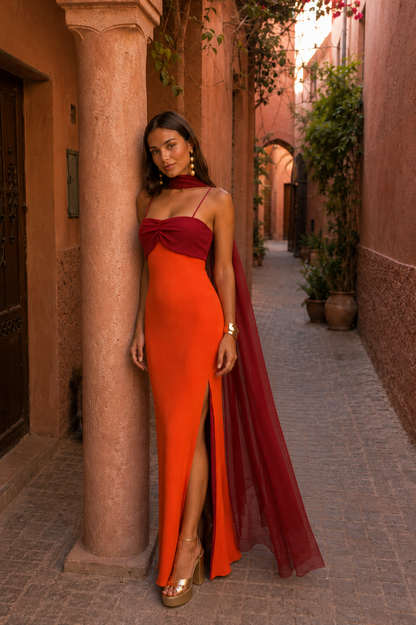 Robe longue orange, buste bordeaux noué, fente avant et voile bordeaux tombant.