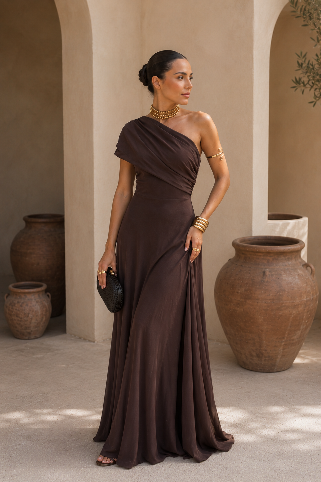 Robe longue marron foncé à une épaule, drapés sur le buste, ourlet fluide évasé.