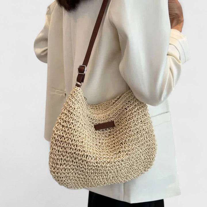 Sac élégant en paille beige, porté à l’épaule, anse marron et ouverture zippée visible.